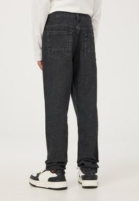 Jeans grigi scuri con una vestibilità rilassata, dotati di due tasche posteriori e orli risvoltati. Indossati con sneakers nere e bianche.
