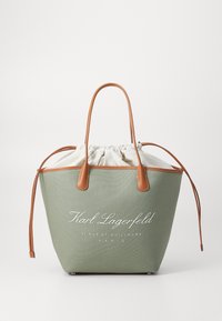 Grønn lerrets totebag med brune lærdetaljer, snøring og hvit tekstlogo. Har en strukturert, rund form.