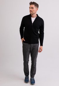 Musta vetoketjullinen takki valkoisen T-paidan päällä, yhdistettynä harmaisiin housuihin ja sinisiin lenkkareihin, valmistettu pehmeästä kankaasta, joka on istuvaa muotoilua.