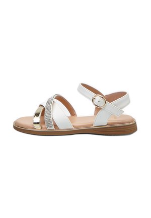Sandali bianchi con cinturini incrociati, fibbia regolabile alla caviglia, dettagli metallici e una fascia scintillante. Suola piatta con bordo marrone chiaro.