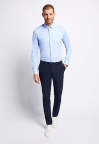 Lichtblauwe overhemd met lange mouwen en knoopsluiting, gecombineerd met donkerblauwe broek en witte sneakers. Soepele stof met een getailleerd ontwerp.