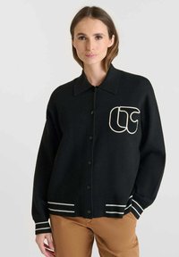 Cardigan nero in lana con colletto, dettagli a righe bianche su polsini e orlo, dotato di un grande logo ricamato sul petto.