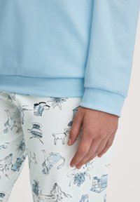 Lichtblauwe sweatshirt gecombineerd met witte broek met een blauw geïllustreerd patroon van dieren en voorwerpen. Zachte stof, ontspannen pasvorm.