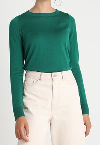 Teal långärmad sweater med rund halsringning, ribbade mudd och jämn textur, i kombination med hög midja ljusbeiga jeans.