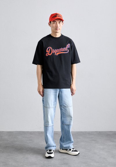 Svart t-skjorte med kort erme og rødt og blått "Dsquared²"-logo, sammen med lyseblå denimjeans og svart-hvite sneakers. Rød caps på hodet.