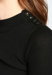 Maglione nero a coste con colletto alto e bottoni decorativi lungo la spalla. Texture morbida, design aderente.