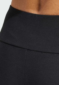 Tessuto a coste nero con una vita ampia e una superficie liscia. Presenta una cucitura che corre orizzontalmente attraverso il punto medio.