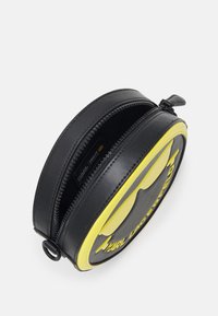 Okrągła czarno-żółta torba z gładką skórzaną powierzchnią, dwoma zamkami błyskawicznymi oraz tłoczonym logo na przodzie.