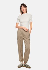 White ribbed short-sleeve top paired with beige cargo pants featuring elastic cuffs, and patterned sneakers in black and white.