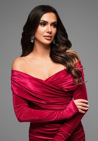 Abito in velluto rosso con design off-the-shoulder e maniche lunghe; presenta drappeggi arricciati e tessuto testurizzato; abbinato a orecchini statement.