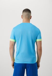 Camiseta deportiva de manga corta de color azul claro con textura de malla y acentos en verde neón en los puños, vista desde la parte posterior.