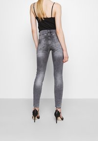 Jeans ajustados de cintura alta en gris con un acabado desgastado, que cuentan con bolsillos traseros y detalles de costura sutiles, combinados con zapatos de tacón negros.