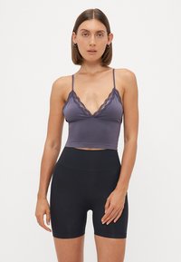 Paarse bralette met kantafwerking en verstelbare bandjes, gecombineerd met hoge zwarte shorts van een gladde, rekbare stof.