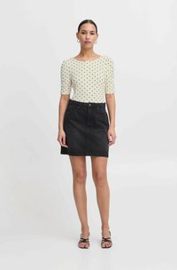 Blusa crema con pois neri, maniche a palloncino corte. Mini gonna di jeans nera con tasche frontali, design semplice, orlo rifinito.