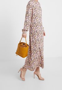 Maxiklänning med ett rosa och beige bladmönster, samlade muddar, kompletterad med en senapsgul bucketväska och ljusrosa remsandaler.