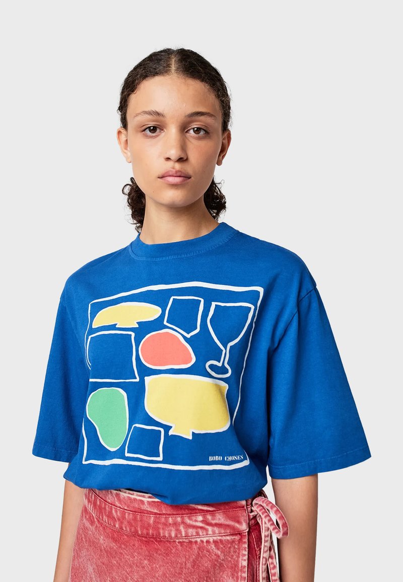 Modrá bavlněná tričko s oversized střihem, s barevnými abstraktními tvary v červené, žluté, zelené a černých konturách na přední straně.