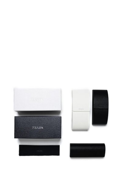 Due scatole rettangolari, una nera e una bianca, con il logo "PRADA" in rilievo, accompagnate da sacchetti per lenti neri e bianchi e un panno per la pulizia.