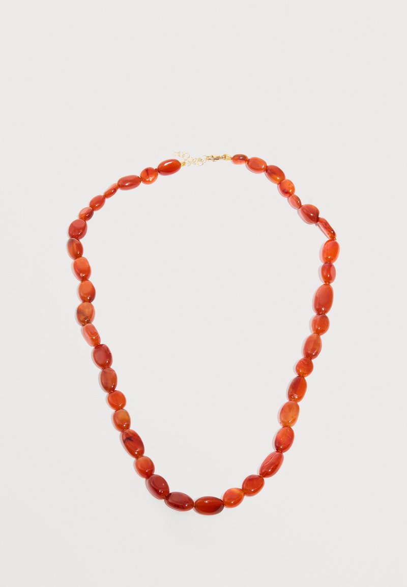 Perles ovales polies de couleur rouge orangé enfilées pour former un collier avec un petit fermoir en or sur un fond blanc uni.
