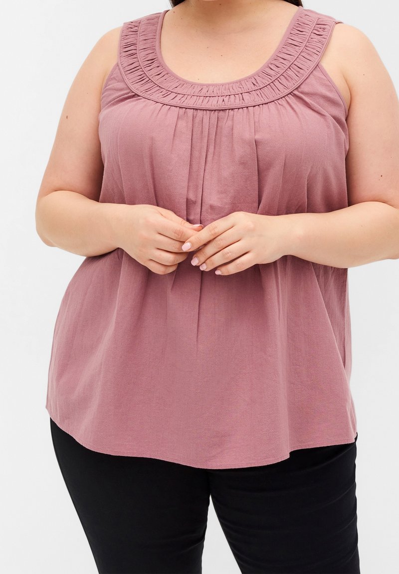 Débardeur à volants rose poussiéreux, avec un col rond orné de détails froncés et une coupe ample, associé à un pantalon noir.