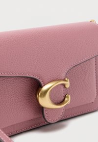 Rózsaszín texturált bőr táska arany színű kapoccsal, kontrasztos varrással és lekerekített sarkokkal rendelkező strukturált kialakítással.