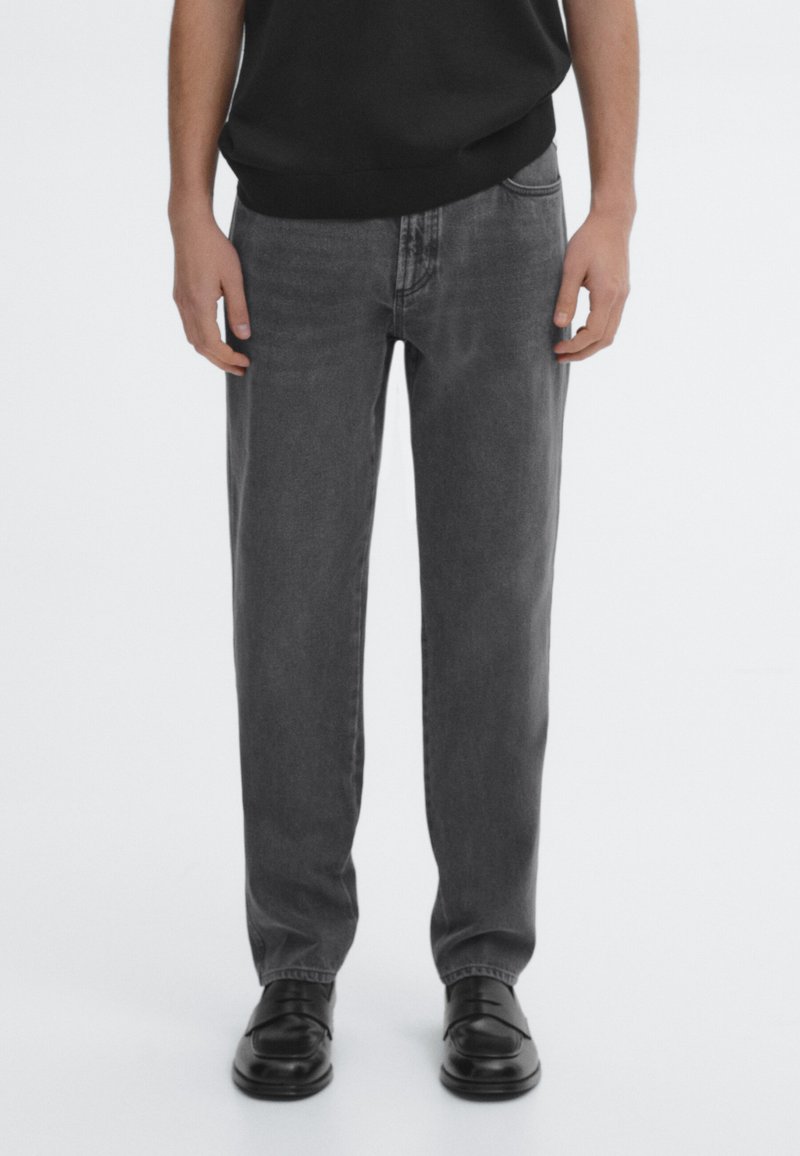 Gray denim jeans with a straight leg cut, featuring five pockets and a classic waistband. Paired with black leather shoes.