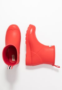 Botas de goma rojas impermeables con una textura suave, punta redonda y suela con un patrón. Cuenta con una pestaña de agarre con una franja de contraste.