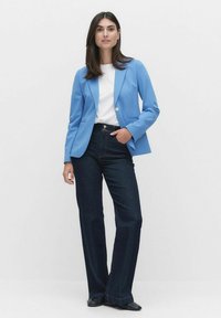 Blå blazer med en enkel knapp, i kombination med en vit skjorta och mörka jeans med utsvängda ben. Svarta skor fulländar outfiten.