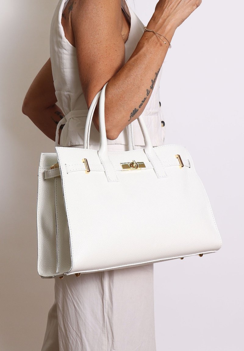 Borsa in pelle bianca con forma strutturata. Presenta hardware dorato e manici doppi. Texture liscia con design minimalista e senza motivi.