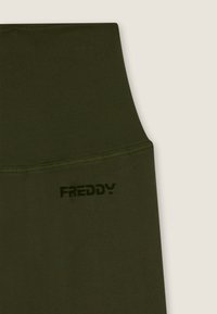 Tumma oliivinvihreät leggingsit, joissa korkea vyötärökaitale. Niissä on teksturoitu kangas ja sivussa hienovarainen musta "FREDDY"-logo.