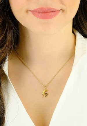 Collier en or avec un pendentif en forme de "G" circulaire, suspendu à une chaîne délicate, porté sur un blouse blanche à col. Fini lisse et poli.