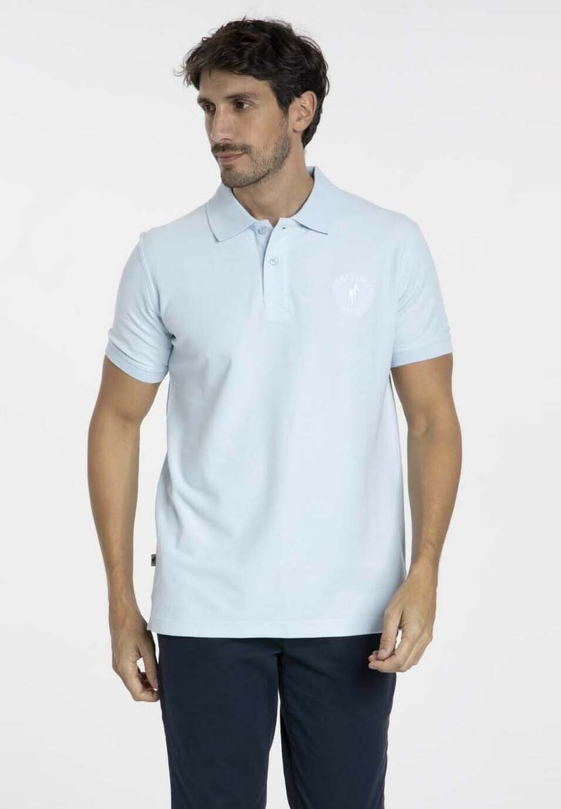 Polo bleu clair à manches courtes, avec un col classique et un petit logo blanc sur la poitrine. Fabriqué en tissu lisse et respirant.