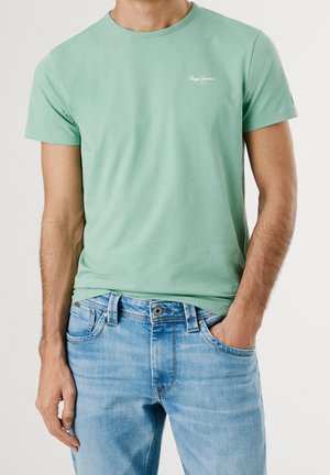T-shirt en coton vert menthe à manches courtes, col rond, avec un petit logo blanc sur la poitrine, associé à un jean en denim bleu clair.