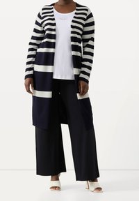 Námořnicky modrý a bílý pruhovaný svetr na zapínání s dlouhými rukávy, otevřeným předním dílem, ve spojení s bílou košilí a širokými černými kalhotami. Hladká texturovaná látka.