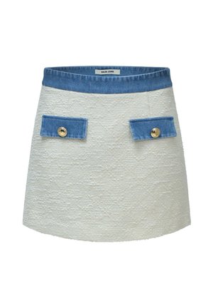 Mini-jupe blanche texturée avec ceinture en denim bleu et rabats de poche, chaque rabat de poche étant sécurisé par un bouton doré.