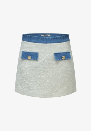 Minifalda blanca texturizada con cintura de mezclilla azul y solapas de bolsillo, cada solapa de bolsillo asegurada con un botón dorado.