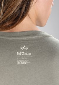 Camisa de color verde oliva con cuello redondo, que muestra texto impreso en blanco y un logotipo en la parte posterior. Tela de algodón suave con un corte estándar.