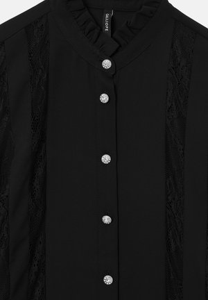 Schwarze Bluse mit einem Rüschenkragen, Spitzen-Seiteneinsätzen und fünf mit Juwelen besetzten Knöpfen auf der Vorderseite. Glattes Material mit strukturierter Optik.