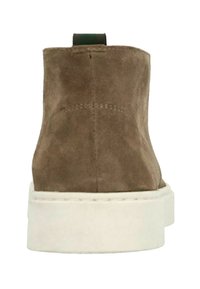Bruine suede enkelboot met een witte rubberen zool, met een groene lus aan de achterkant voor gemakkelijk aan- en uittrekken, en nette stiksels.