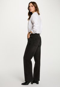 Jeans negros de pierna recta hechos de denim, con cinco pockets, costuras sutiles y una cintura alta, combinados con una camisa blanca de botones.