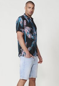 Camisa negra de manga corta con estampado de palmeras en rosa y azul, combinada con pantalones cortos de mezclilla azul claro, con un ajuste relajado y estilo casual.