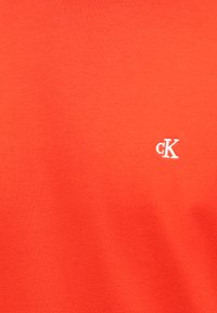 Pomarańczowa bawełniana koszulka, z małym białym haftowanym logo "CK" po lewej stronie, gładka w dotyku i o swobodnym kroju.