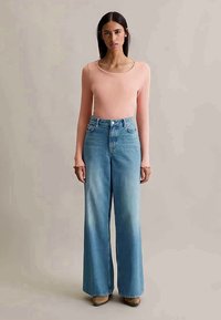 Ανοιχτό ροζ ριγέ μπλούζα με μακριά μανίκια, συνδυασμένη με ανοιχτό μπλε φαρδιά τζιν παντελόνια. Τα τζιν έχουν ψηλή μέση και μια διακριτική φθορά.