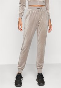 Grå, fløyelsmyke joggebukser med elastisk midje og snor; tettsittende mansjetter ved anklene. Brukt med svarte joggesko.