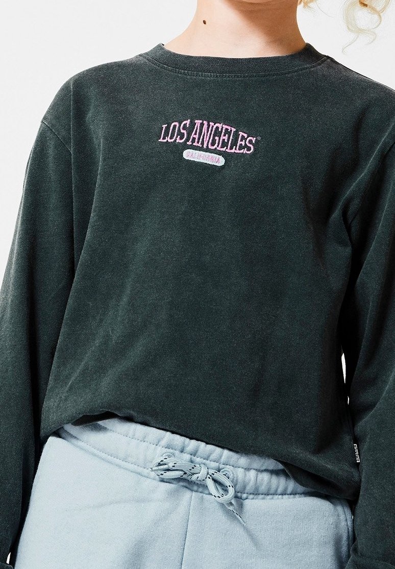 Enfant portant un t-shirt à manches longues vert foncé avec le texte "Los Angeles California" et un pantalon de survêtement bleu clair avec une taille à cordon.