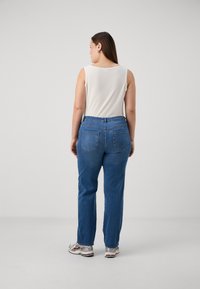 Blue denim jeans with a relaxed fit, featuring back pockets, paired with a white ribbed tank top. The person's shoes are silver sneakers.