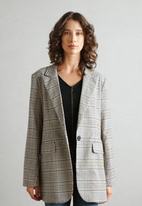 Överdimensionerad rutiga kavaj i grått, beige och svart, med skarpa slag, två framfickor och en enkel knappstängning. Texturerad tyg.