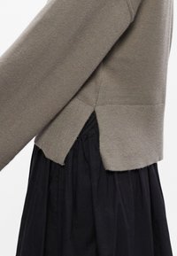 Szary, dzianinowy sweter z długimi rękawami, z bocznym rozporkiem i prążkowanym dołem, zestawiony z czarną, teksturowaną spódnicą w warstwach.