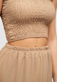 Beige tweed set bestaande uit een smocked crop top en een bijpassende rok met elastische taille. De stof heeft een zachte, textuurafwerking.