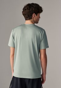 Camiseta deportiva verde claro hecha de tejido transpirable, con mangas cortas y una superficie texturizada, combinada con pantalones cortos oscuros.