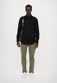 Svart langermet skjorte med knapplukking, olivengrønne bukser, hvite sneakers og en svart crossover-veske med stropp. Minimalistisk stil.